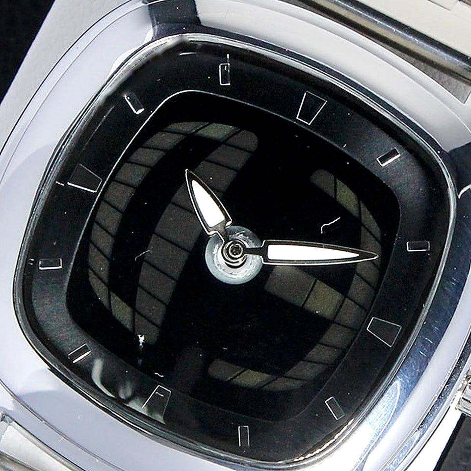 Gros plan sur le cadran noir de la TIMELOOM 01 Coussin : grille 3D bombée, index bâtons et aiguilles blanches